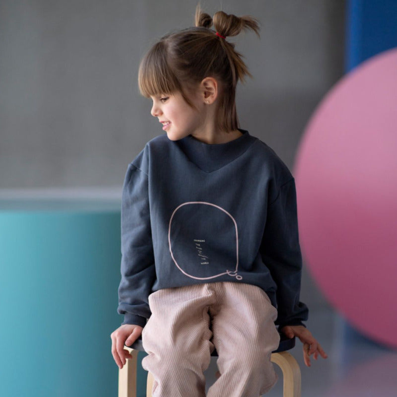 Una bellissima felpa in caldo cotone biologico sui toni del blu notte e con la scritta rosa"Changing the rules and re-inventing the world". Apertura retro collo con bottoncini a pressione, scollo rotondo a costine, elastico in vita e sulle maniche.