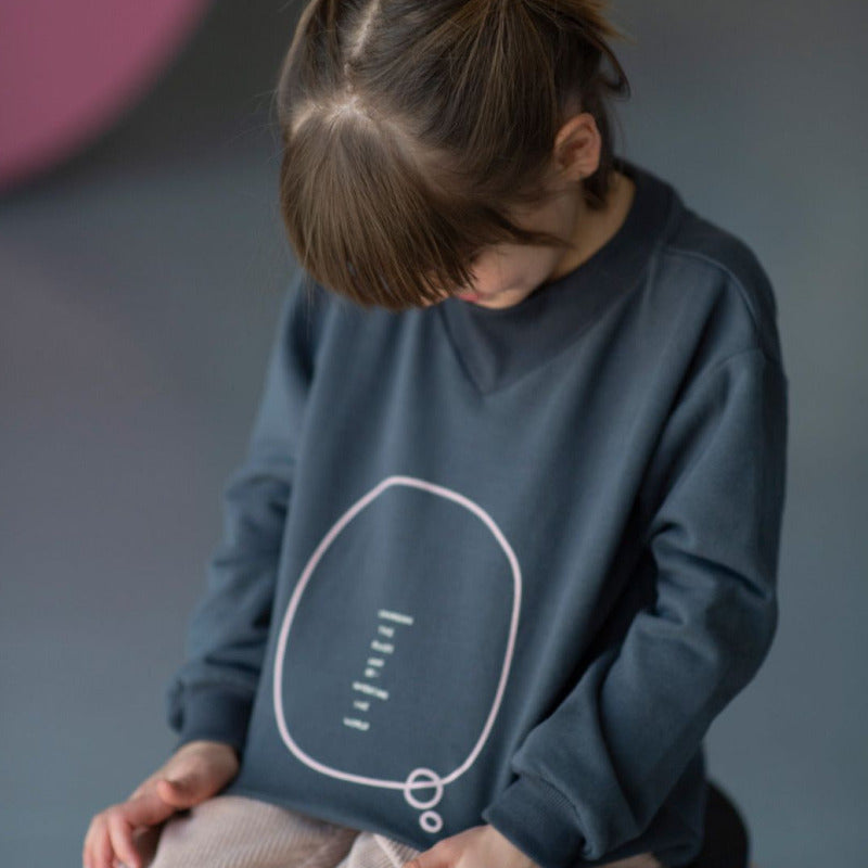 Una bellissima felpa in caldo cotone biologico sui toni del blu notte e con la scritta rosa"Changing the rules and re-inventing the world". Apertura retro collo con bottoncini a pressione, scollo rotondo a costine, elastico in vita e sulle maniche.