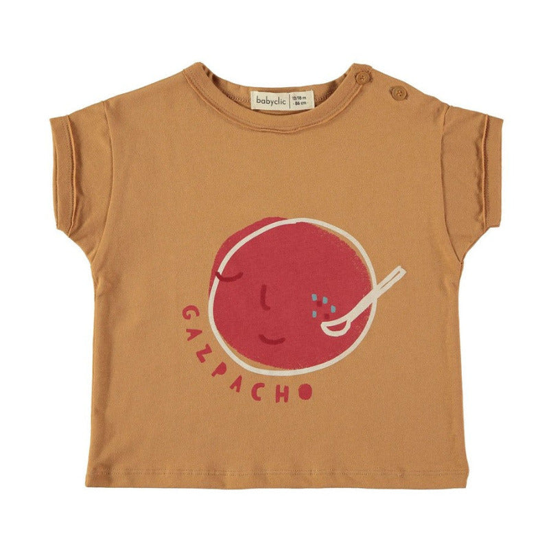 Una bellissima t-shirt per i vostri bambini in morbido e fresco cotone biologico a manica corta, con la stampa di una grande gazpacho su fondo caramello. Apertura lungo spalla tramite bottoncini.