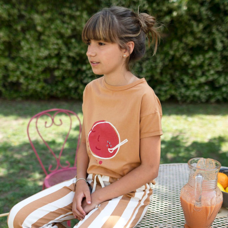 Una bellissima t-shirt per i vostri bambini in morbido e fresco cotone biologico a manica corta, con la stampa di una grande gazpacho su fondo caramello. Apertura lungo spalla tramite bottoncini.