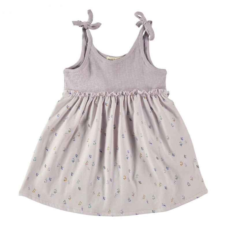Grazioso abito bambina in morbido e leggero cotone biologico con fantasia a fiori su fondo lavanda. Elastico in vita con rifinitura arricciata, corpetto con trama a costine, spalline con chiusura a nodo. 