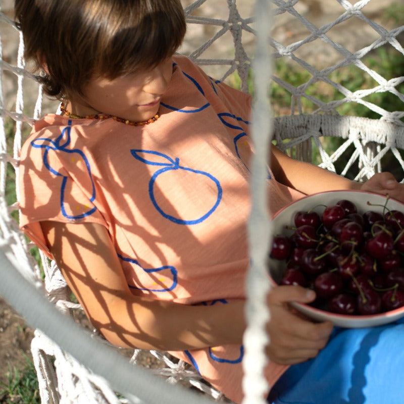 t-shirt bambini in cotone biologico a manica corta, con tanti frutti blu su fondo arancio. Finiture con bordi grezzi